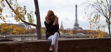 Paris geçmişi olan cep telefonu kullanan bir kız, Seine nehri ve Eyfel kulesi..