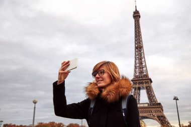 Paris geçmişi ve Eyfel kulesi olan cep telefonu kullanan bir kız..