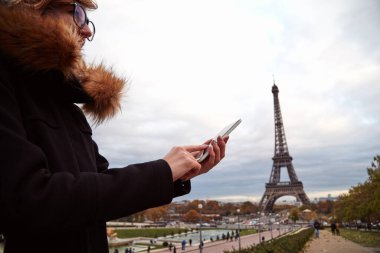 Paris geçmişi ve Eyfel kulesi olan cep telefonu kullanan bir kız..