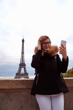 Paris geçmişi ve Eyfel kulesi olan cep telefonu kullanan bir kız..