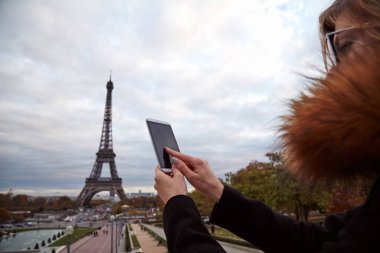 Paris geçmişi ve Eyfel kulesi olan cep telefonu kullanan bir kız..