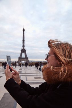 Paris geçmişi ve Eyfel kulesi olan cep telefonu kullanan bir kız..