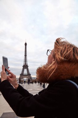 Paris geçmişi ve Eyfel kulesi olan cep telefonu kullanan bir kız..