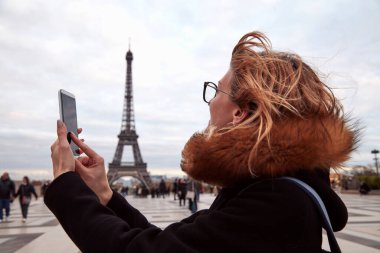 Paris geçmişi ve Eyfel kulesi olan cep telefonu kullanan bir kız..