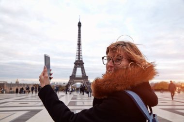 Paris geçmişi ve Eyfel kulesi olan cep telefonu kullanan bir kız..