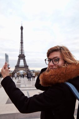 Paris geçmişi ve Eyfel kulesi olan cep telefonu kullanan bir kız..