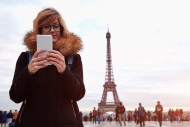Paris geçmişi ve Eyfel kulesi olan cep telefonu kullanan bir kız..