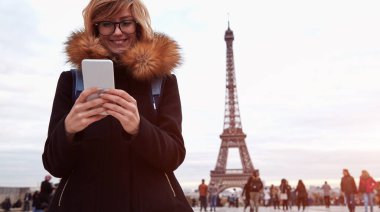 Paris geçmişi ve Eyfel kulesi olan cep telefonu kullanan bir kız..