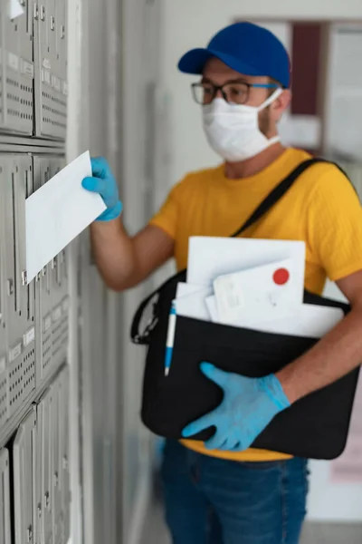 Mailman delivering mail with mail-bag and protective mask and gloves during virus pandemic.