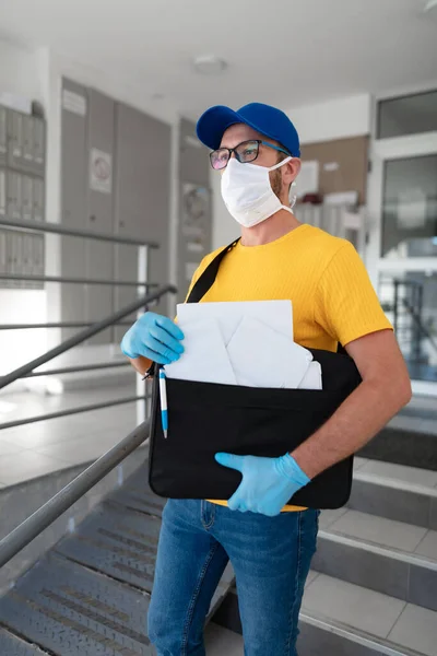 Mailman delivering mail with mail-bag and protective mask and gloves during virus pandemic.
