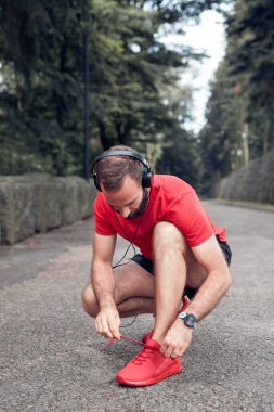 Sportif yetişkin adam parkta koştuktan ve egzersiz yaptıktan sonra ara veriyor ve koşu ayakkabılarını bağlıyor..