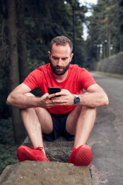 Parkta spor yaptıktan sonra cep telefonu kullanan modern sporcu..