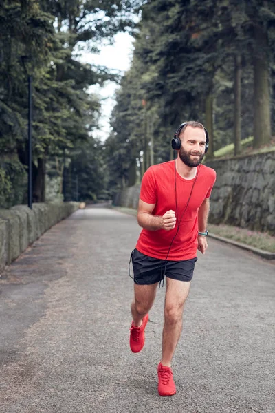 Sportif yetişkin adam parkta koşup egzersiz yaptıktan sonra duraklıyor..