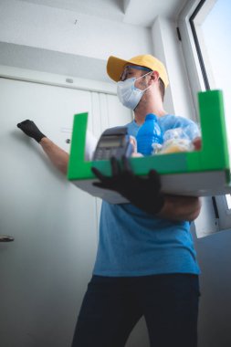 Koruyucu maskeli teslimatçı. Bakkaliye ve POS 'la dolu bir çanta tutuyor..