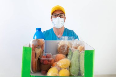 Koruyucu maskeli teslimatçı. Bakkaliye kutusuyla birlikte..