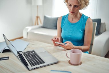 Evden çalışan bir kadın, dizüstü bilgisayar ve cep telefonu kullanıyor, modern serbest çalışma kavramı..