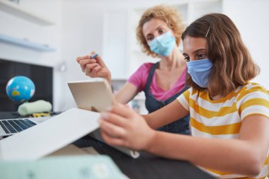 Virüsler, grip ve mevsimsel salgın zamanında özel öğretmen / koruyucu maskeli bir anneyle evde eğitim görüyor..