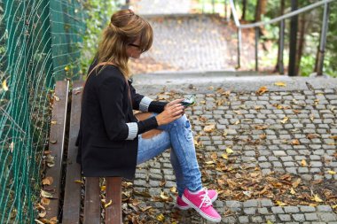 Genç beyaz kadın modern akıllı telefonu sokakta tutuyor..