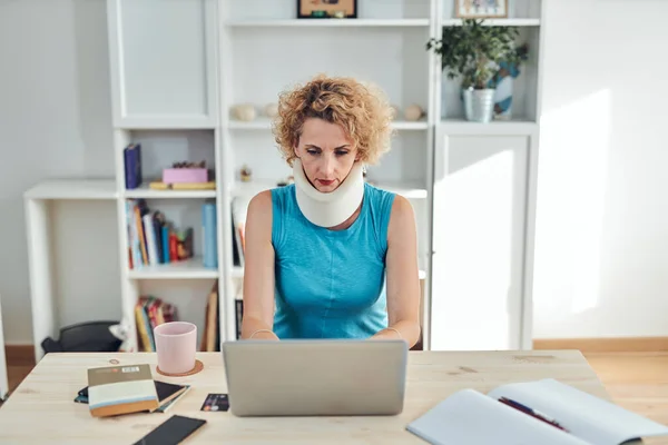 Woman with neck / cervical collar and neck / spinal injury working at home on a laptop.
