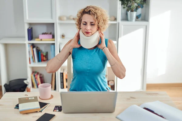 Woman with neck / cervical collar and neck / spinal injury working at home on a laptop.