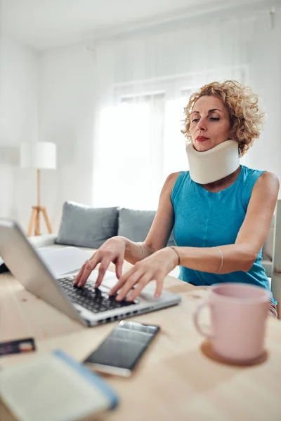 Woman with neck / cervical collar and neck / spinal injury working at home on a laptop.