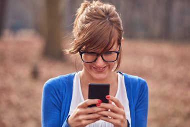 Sonbahar parkında akıllı telefon kullanan genç bir kadın..