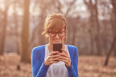 Sonbahar parkında akıllı telefon kullanan genç bir kadın..