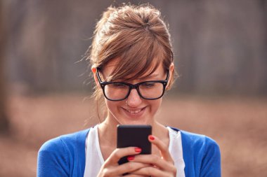 Sonbahar parkında akıllı telefon kullanan genç bir kadın..