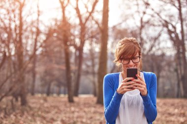 Sonbahar parkında akıllı telefon kullanan genç bir kadın..