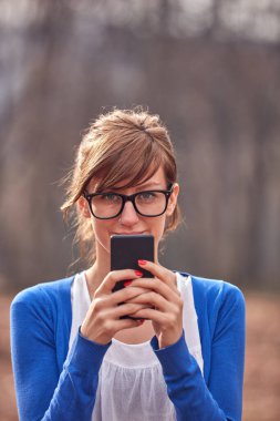 Sonbahar parkında akıllı telefon kullanan genç bir kadın..