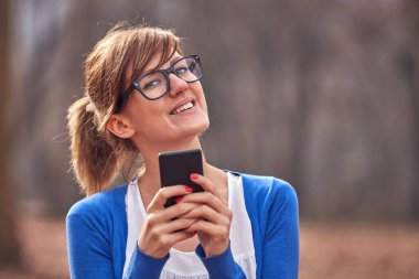 Sonbahar parkında akıllı telefon kullanan genç bir kadın..