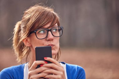 Sonbahar parkında akıllı telefon kullanan genç bir kadın..