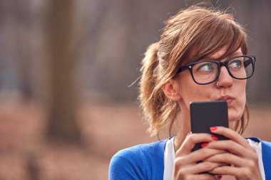 Sonbahar parkında akıllı telefon kullanan genç bir kadın..