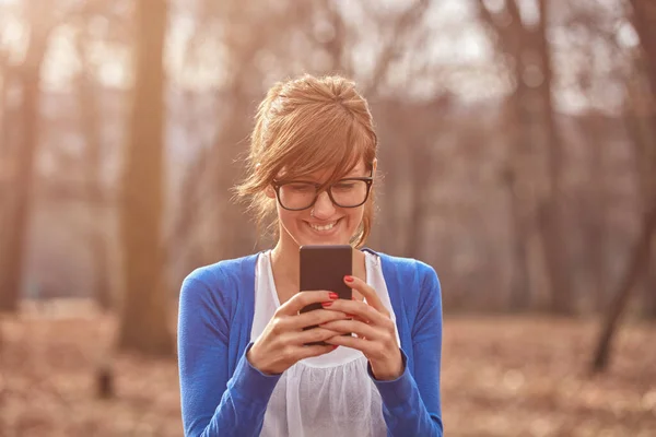 秋の紅葉公園でスマホを使う若い女性 — ストック写真