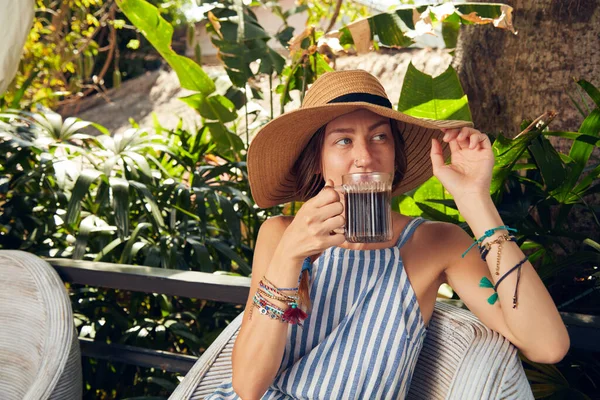 Young caucasian woman sitting on a patio and drinking coffee / tea in summertime season.