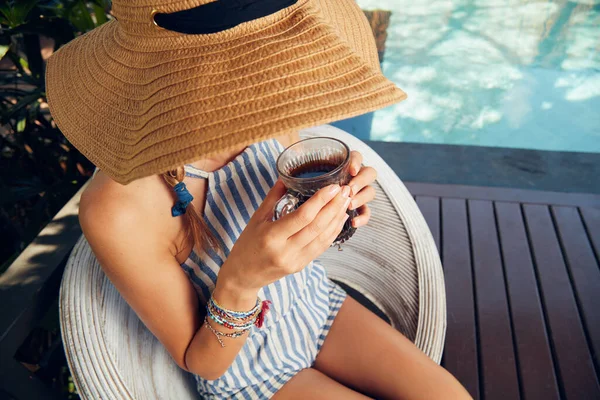 Young caucasian woman sitting on a patio and drinking coffee / tea in summertime season.