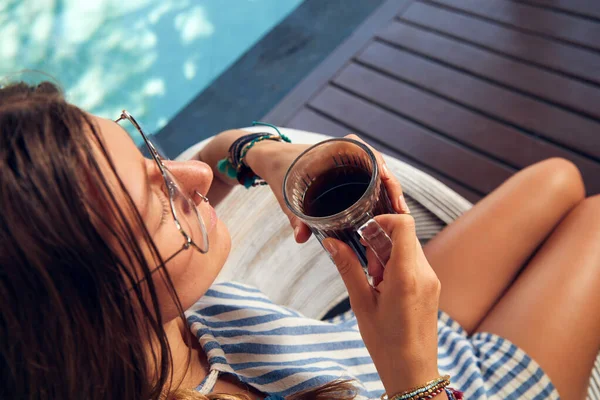 Young caucasian woman sitting on a patio and drinking coffee / tea in summertime season.