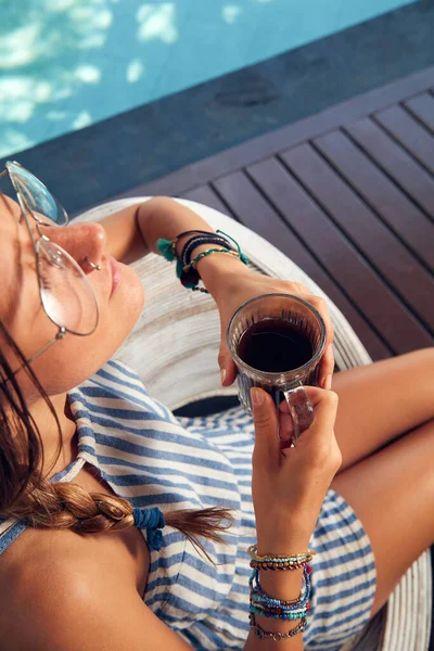 Young caucasian woman sitting on a patio and drinking coffee / tea in summertime season.