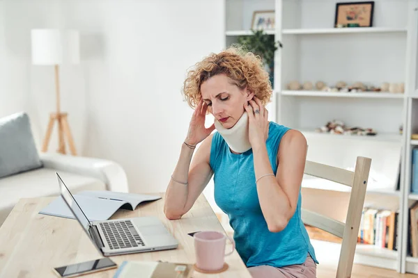 Woman with neck / cervical collar and neck / spinal injury working at home on a laptop.