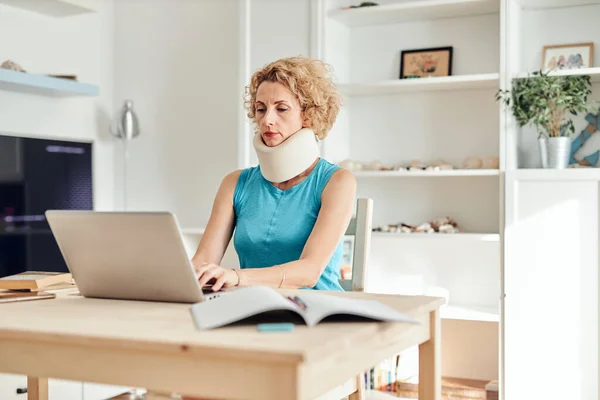 Woman with neck / cervical collar and neck / spinal injury working at home on a laptop.