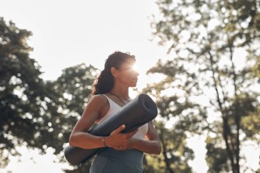 Gün batımında parkta yoga minderi tutan kadın..