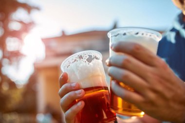 Güneşli bir günde elinde bira bardağı tutan kişi.