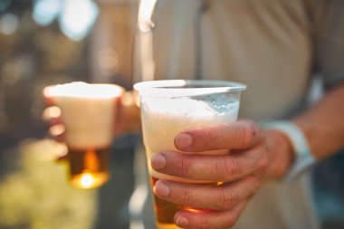 Güneşli bir günde elinde bira bardağı tutan kişi.