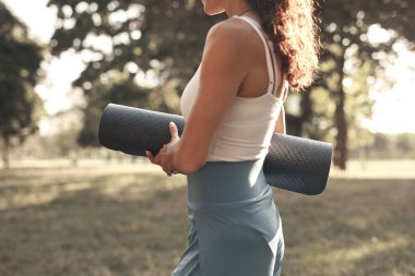 Gün batımında parkta yoga minderi tutan kadın..