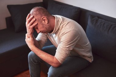 Evdeki kanepede oturan baş ağrısı ve depresyonu olan bir adam..