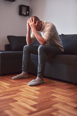 Evdeki kanepede oturan baş ağrısı ve depresyonu olan bir adam..