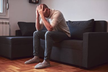 Evdeki kanepede oturan baş ağrısı ve depresyonu olan bir adam..
