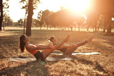Sıcak ve güneşli bir yaz gününde iki kadın parkta yoga yapıyor ve esneme hareketleri yapıyor..