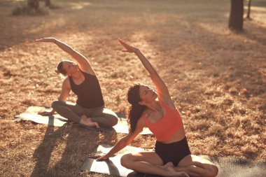 Sıcak ve güneşli bir yaz gününde iki kadın parkta yoga yapıyor ve esneme hareketleri yapıyor..