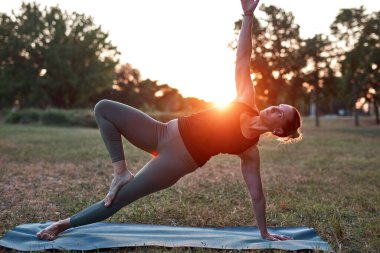 Sıcak bir yaz gününde parkta yoga ve esneme egzersizleri yapan bir kadın..